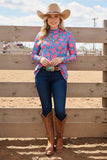 Woman in a colorful top and cowboy hat standing in front of a wooden fence.
