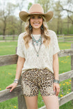 Woman wearing a cowboy hat, lace top, and leopard print shorts outdoors.