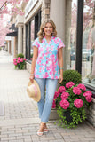 Woman in a floral top and jeans standing on a sidewalk with cherry blossoms and pink flowers.