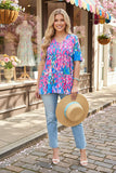 Woman wearing a colorful patterned shirt and straw hat standing on a street with shops in the background.