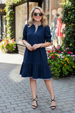 Woman in a navy dress standing on a sidewalk with flowers and storefronts in the background