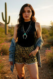 Woman in a desert setting wearing a black top, leopard print shorts, and a denim jacket.