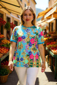 Woman wearing a colorful floral and baroque patterned top in an outdoor market setting.
